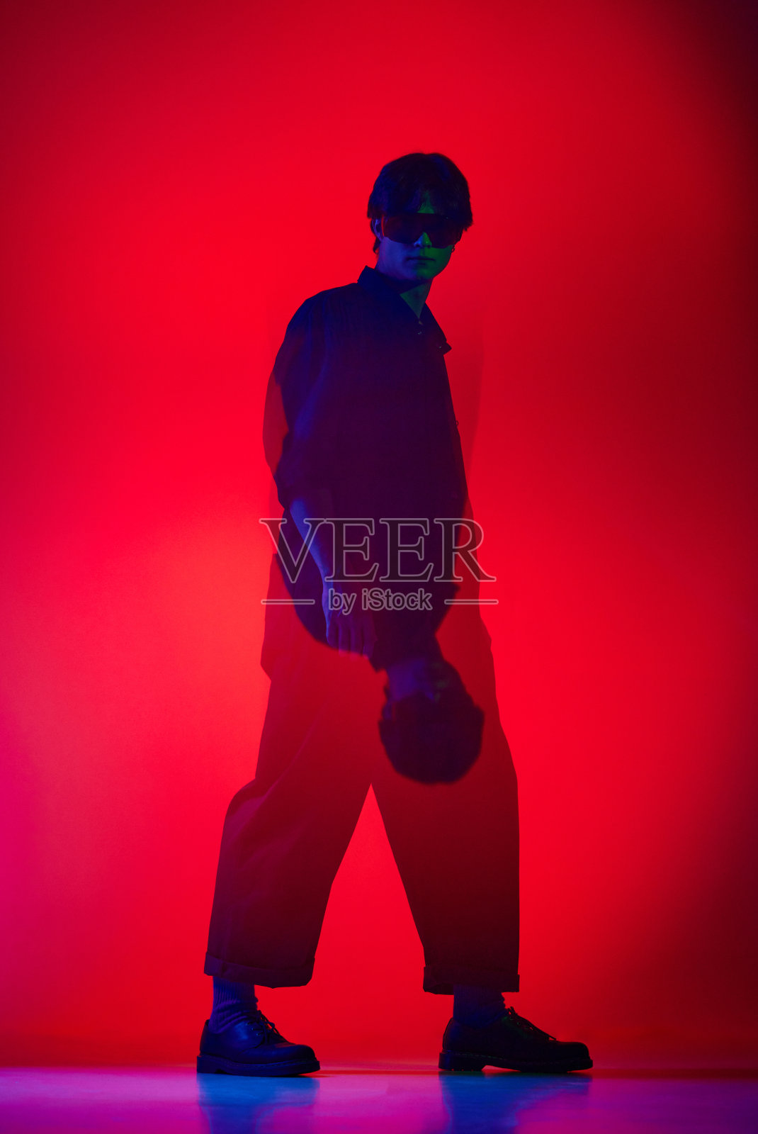 在霓虹灯的红色背景下,穿着连体衣的英俊非凡的年轻人摆姿势。时装表演照片摄影图片