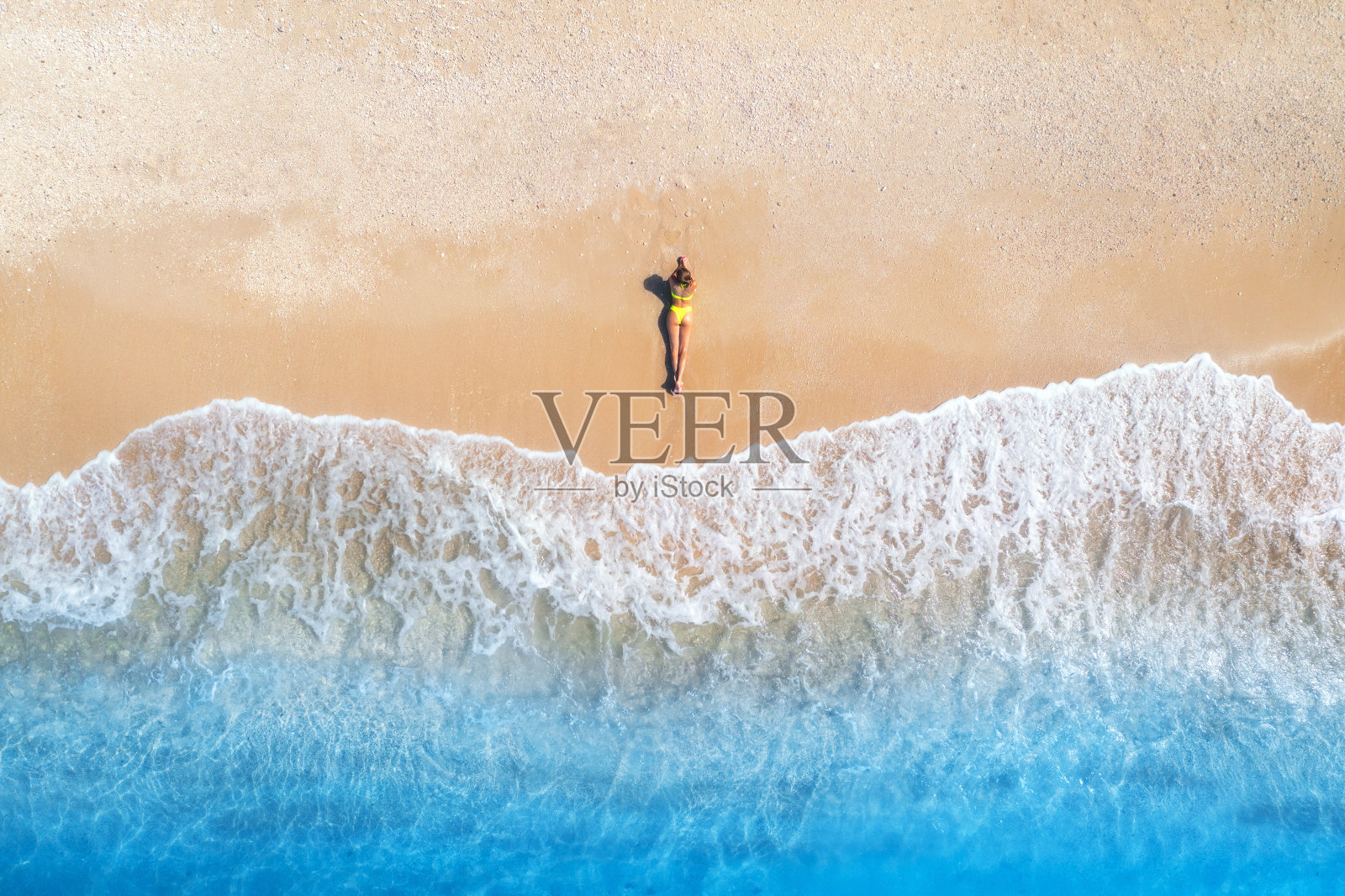 鸟瞰美丽的年轻女子躺在靠近大海的热带沙滩上,日落时有波浪。暑假在希腊莱夫卡达岛。俯视图苗条的女孩,清澈湛蓝的水。海边照片摄影图片