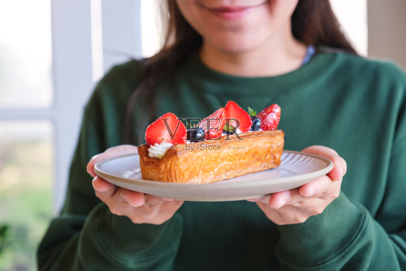 一名年轻女子拿着一盘混合浆果原木羊角面包的特写照片照片摄影图片