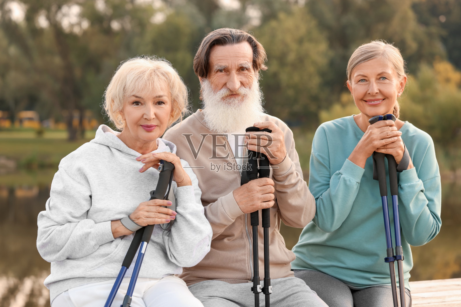 一群老年人带着北欧步行杆坐在室外的木制护墙上照片摄影图片