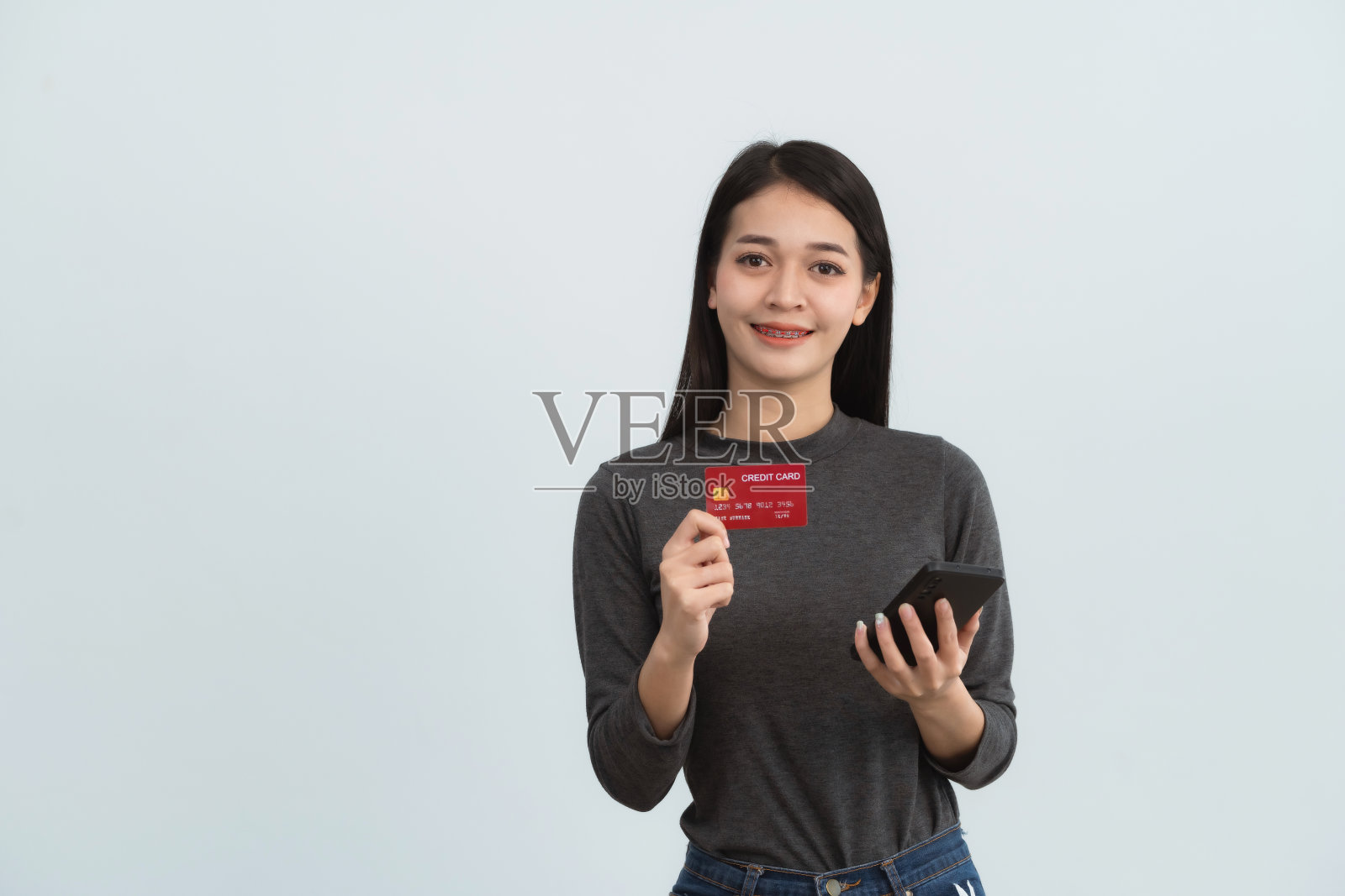 亚洲妇女拿着信用卡和手机在网上购物,孤立在白色或灰色背景的工作室。网上购物,电子商务,网上银行,花钱观念。照片摄影图片