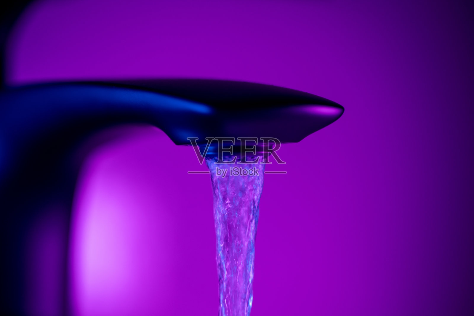 一个优雅的水龙头的特写,水在流动,霓虹灯照明照片摄影图片