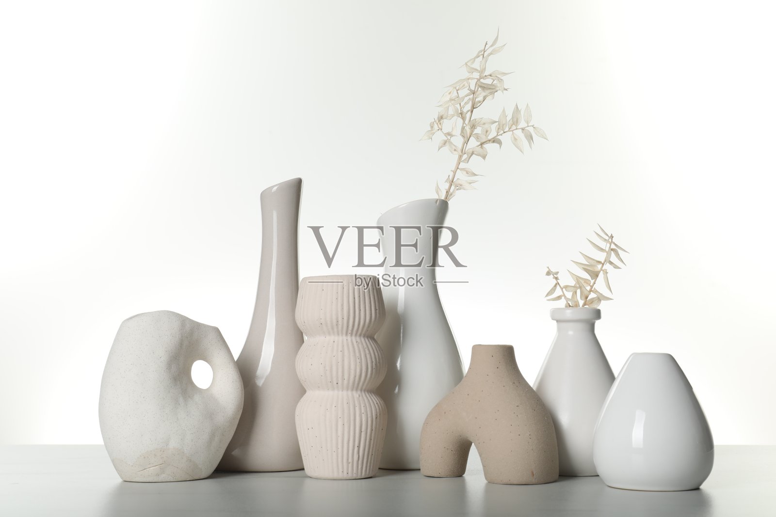 不同风格的花瓶和干花在浅色的桌子上,白色的背景照片摄影图片