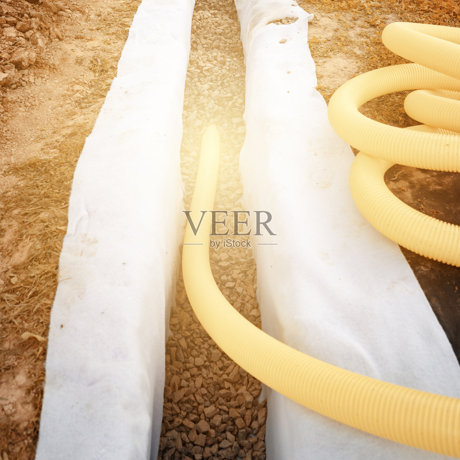 在有碎石和土工织物的沟渠中有穿孔的黄色波纹管。为抽取地下水而进行的排水工程。照片摄影图片