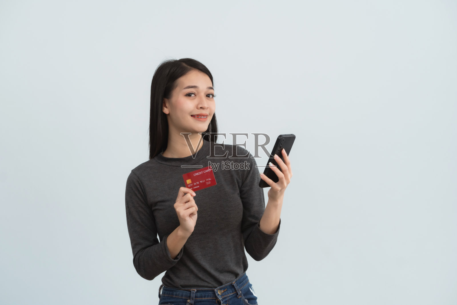 亚洲妇女拿着信用卡和手机在网上购物,孤立在白色或灰色背景的工作室。网上购物,电子商务,网上银行,花钱观念。照片摄影图片
