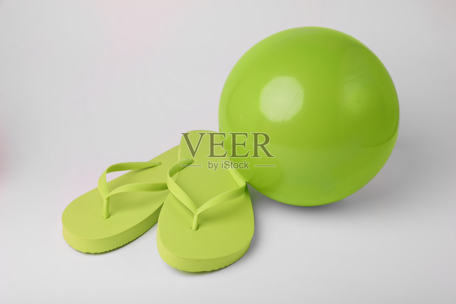白色背景的绿色充气沙滩球和人字拖照片摄影图片