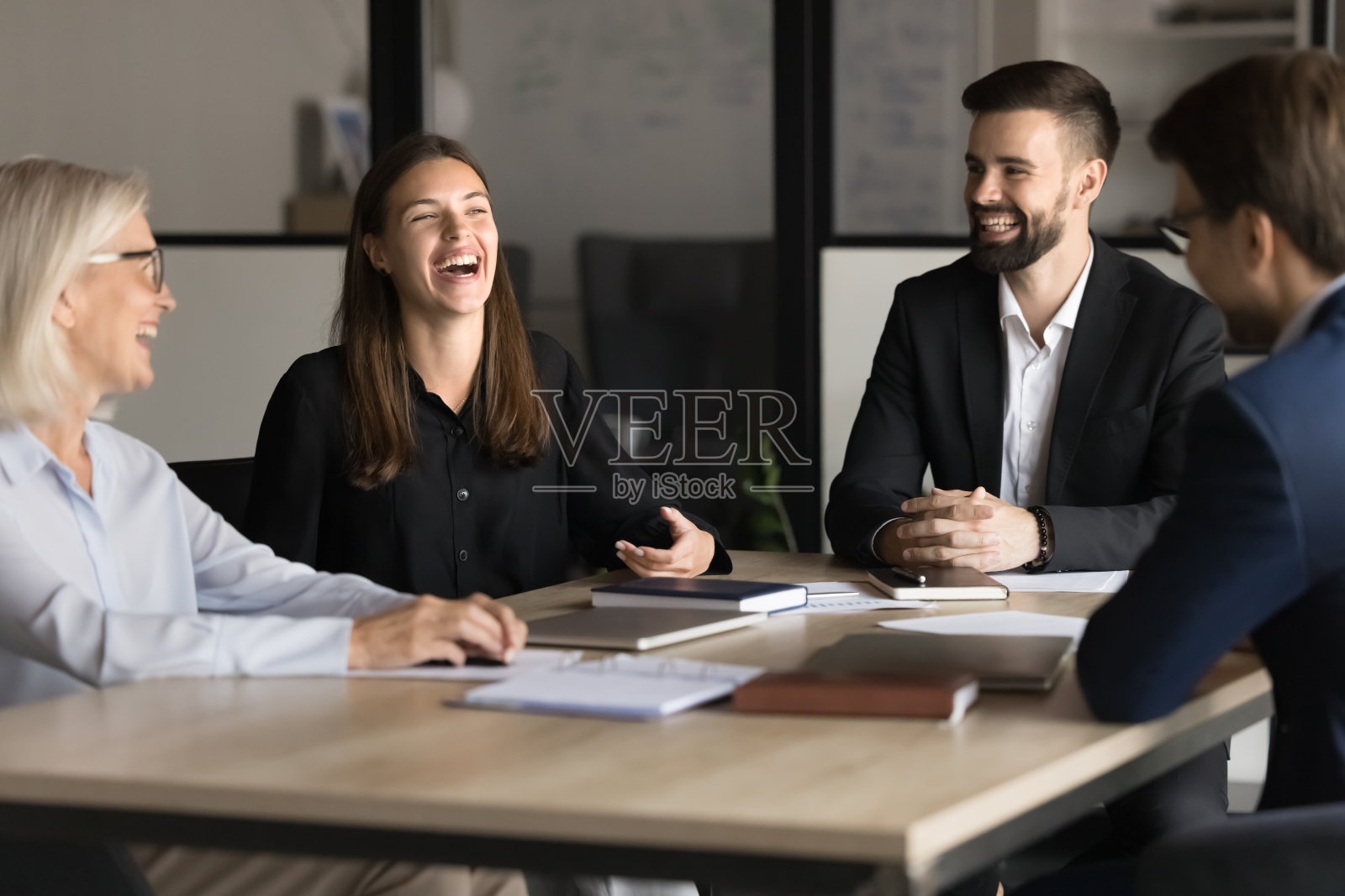 在会议桌上开怀大笑的年轻和年长的同事照片摄影图片