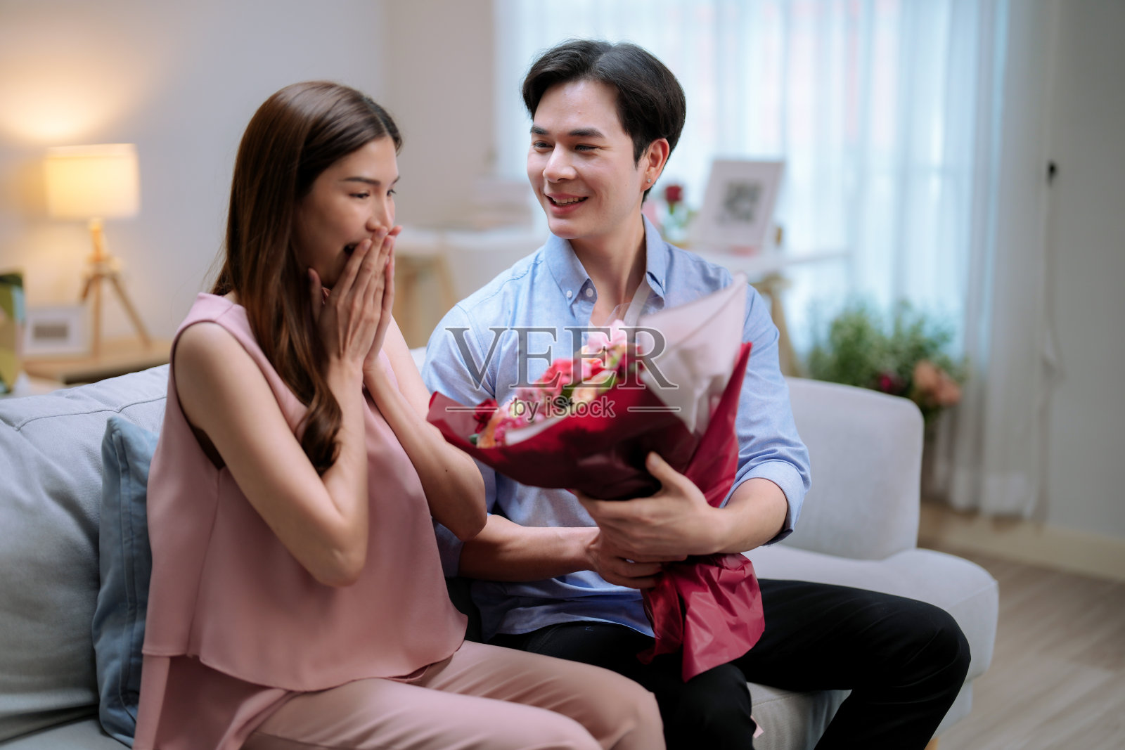 快乐的亚洲夫妇在情人节一起呆在家里,英俊的年轻人用一束美丽的花给他的女朋友一个惊喜。照片摄影图片