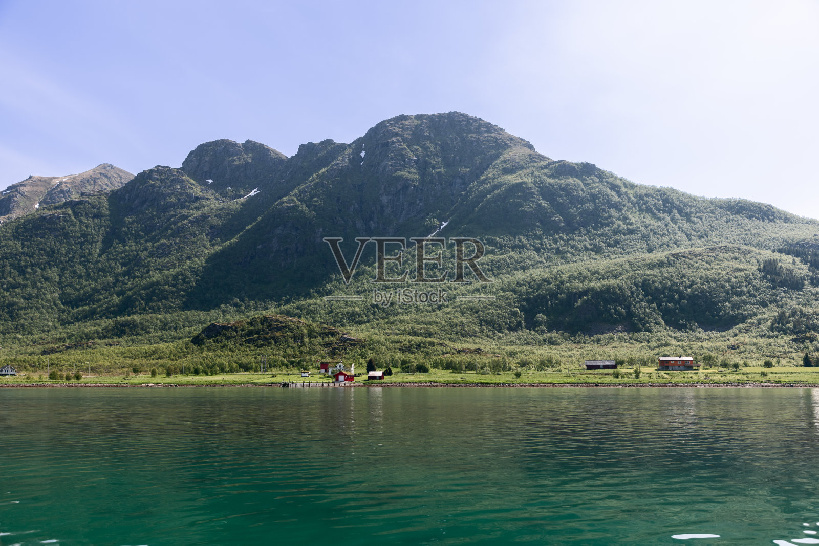 挪威峡湾的宁静碧绿的海水轻轻地拍打着一个僻静的农场的海岸,被罗弗敦高耸的绿色山丘所环绕照片摄影图片