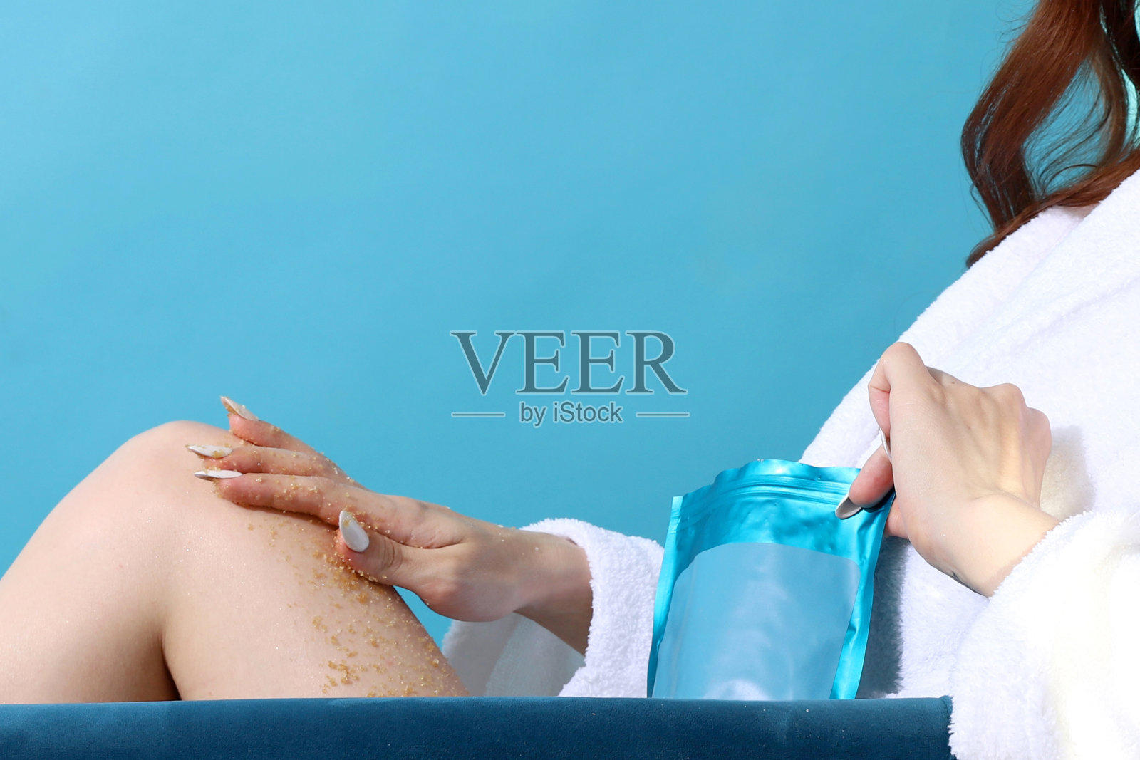 搓洗以清洁皮肤。脚擦洗。女性的美容。蓝色背景。一个穿着白色毛巾布长袍度假的女人。白色修指甲。漂亮整洁的手。高质量的照片摄影图片