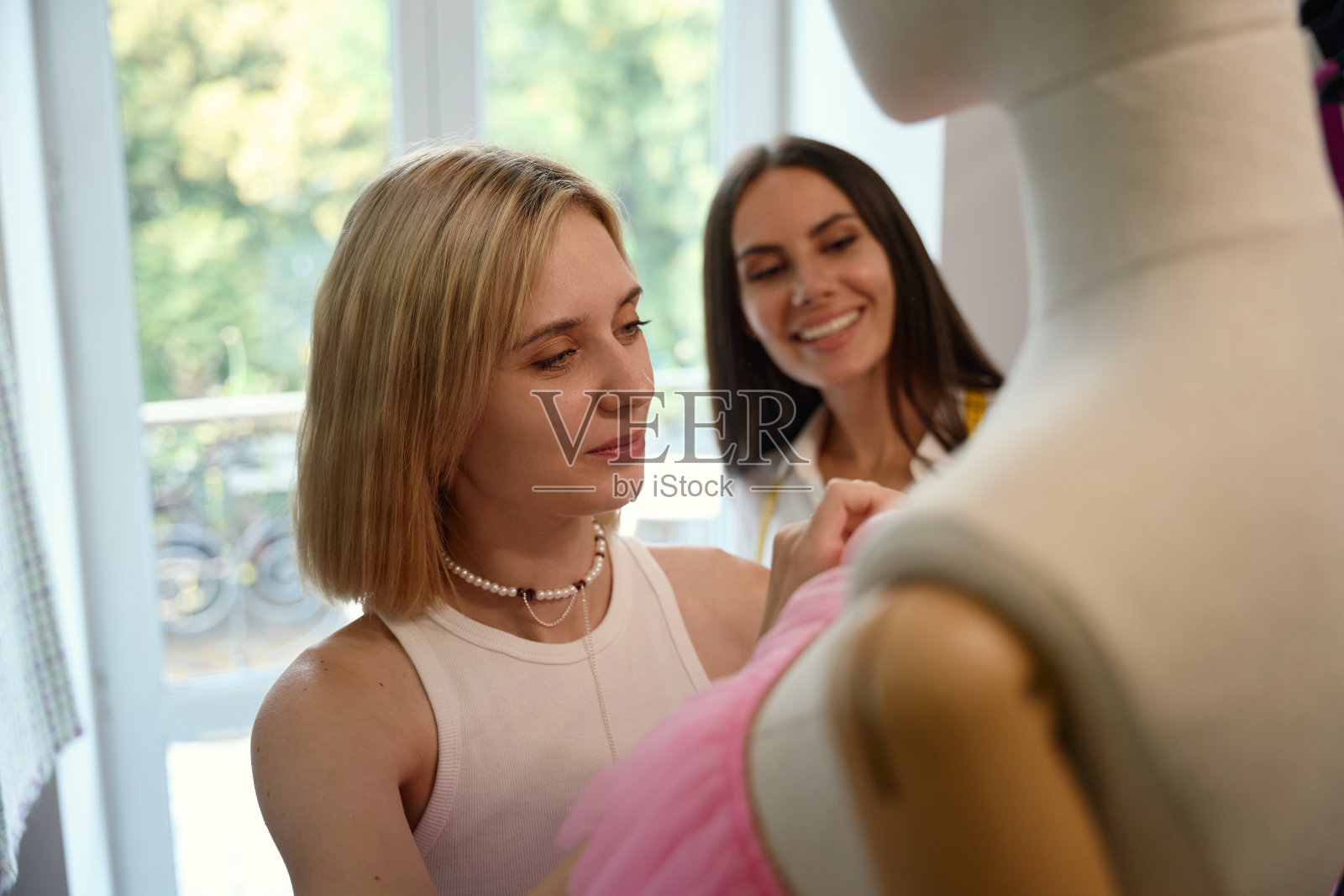 设计工作室里的女人们正在设计一件粉红色的晚礼服照片摄影图片