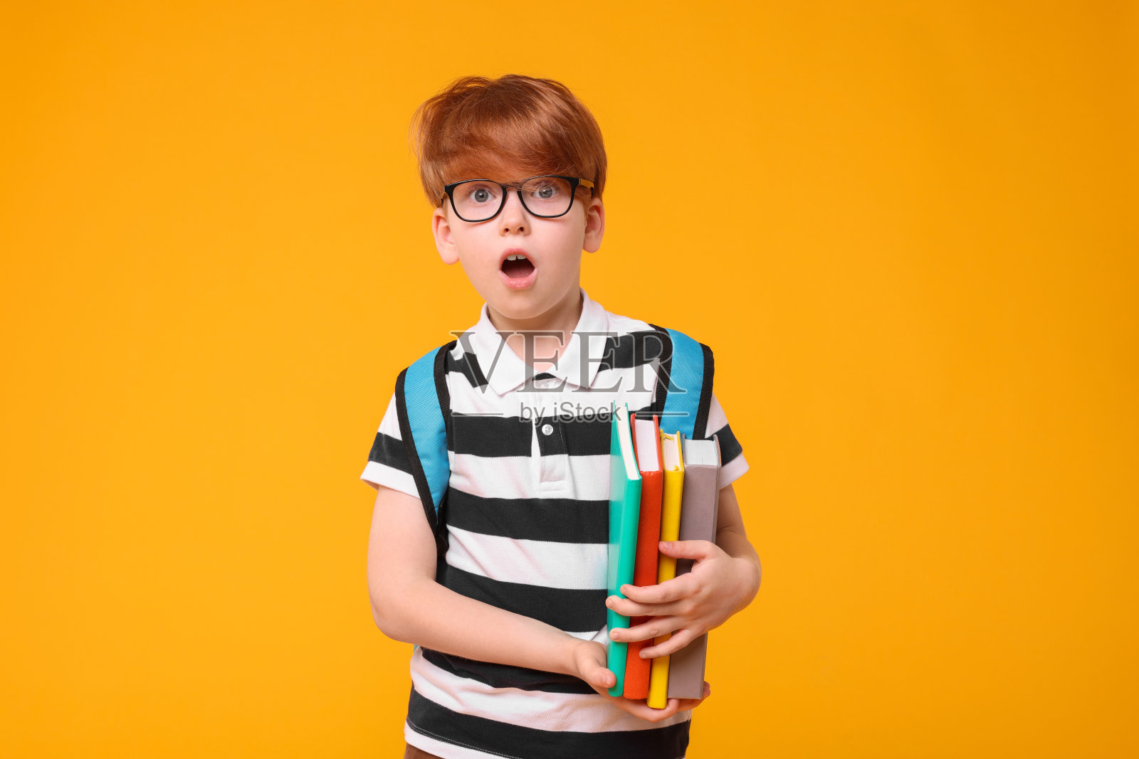 惊讶的男生背着双肩包和橙色背景的书照片摄影图片