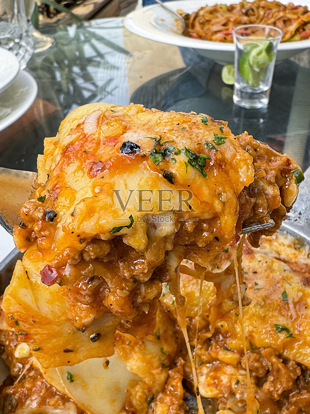 一叉意大利面条的特写图像,从金属处理的盘子中取出,缺了一部分,放在白色盘子上的餐巾纸上,金属餐具,玻璃顶的餐厅餐桌,重点放在前景照片摄影图片