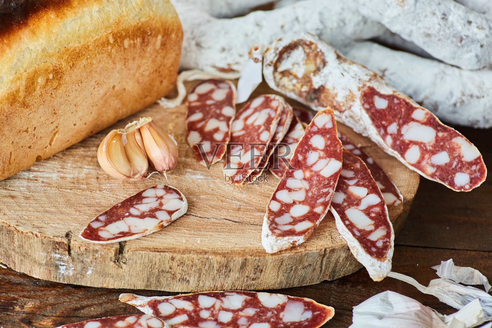 切片的干的或烟熏的带白霉的香肠,放在木桌上,周围是一条白面包。肉类生产。照片摄影图片