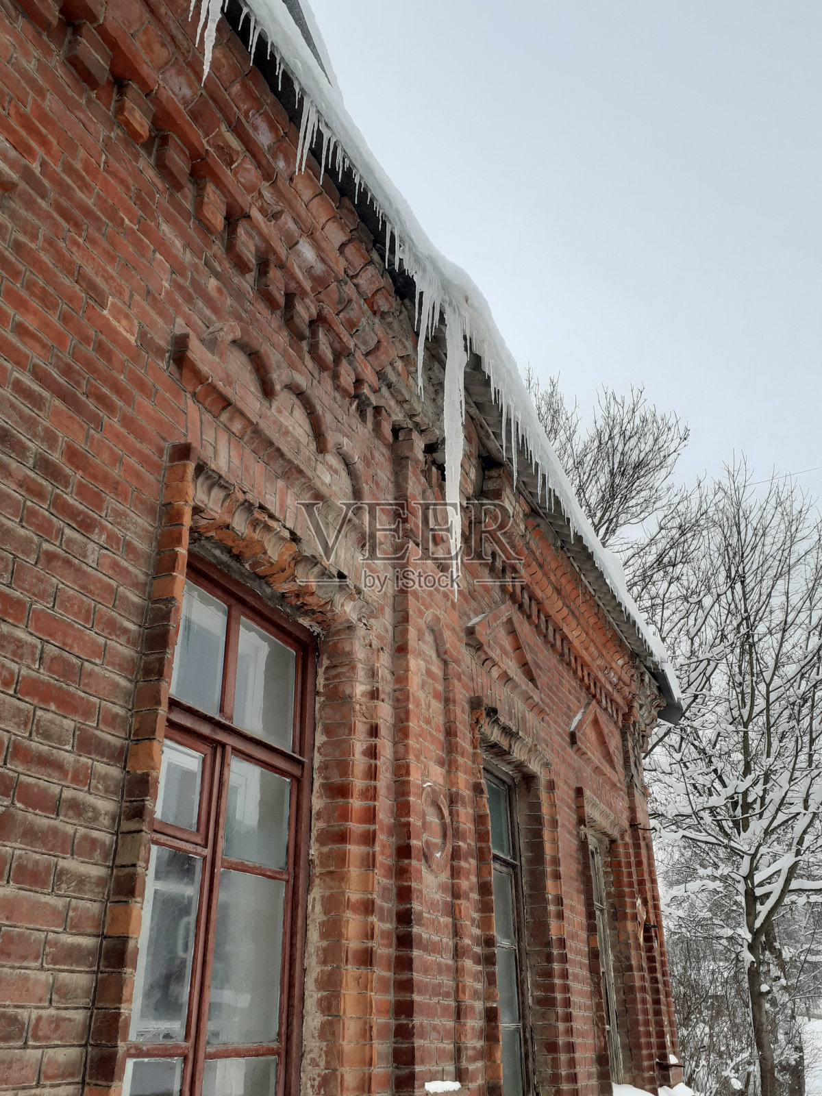 一座古老红砖建筑屋顶上的巨大冰柱。照片摄影图片