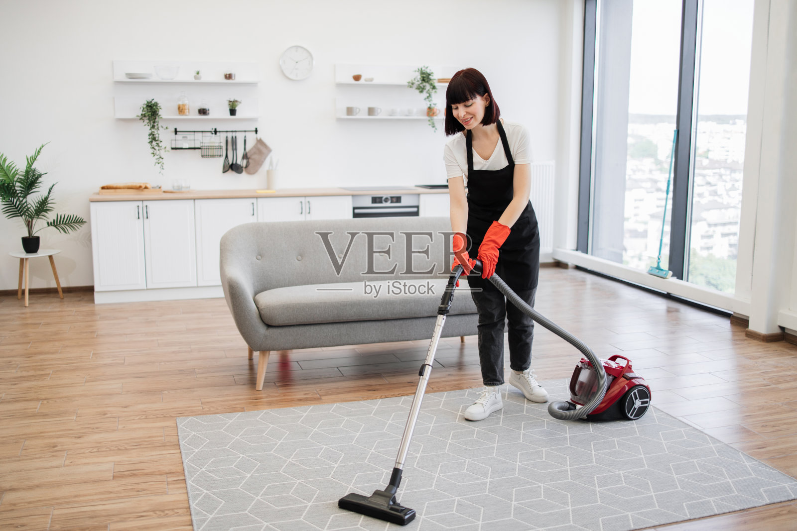 围裙里的专业女清洁工积极打扫现代公寓。照片摄影图片