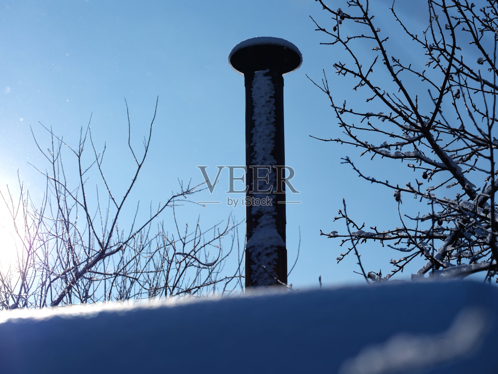 积雪覆盖的屋顶上的旧金属烟囱,背景是降雪后的蓝天。照片摄影图片