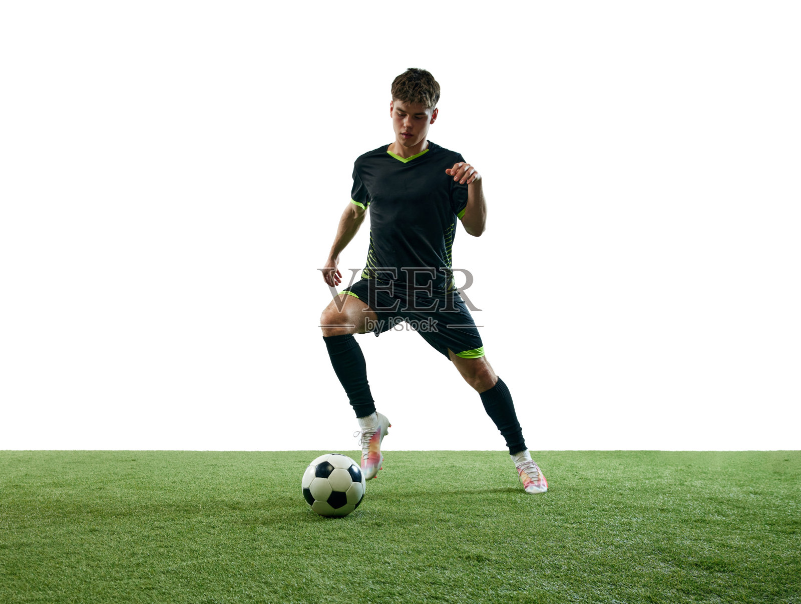 穿着黑色制服的年轻人,足球运动员,在白色背景和草地地板上运球。照片摄影图片