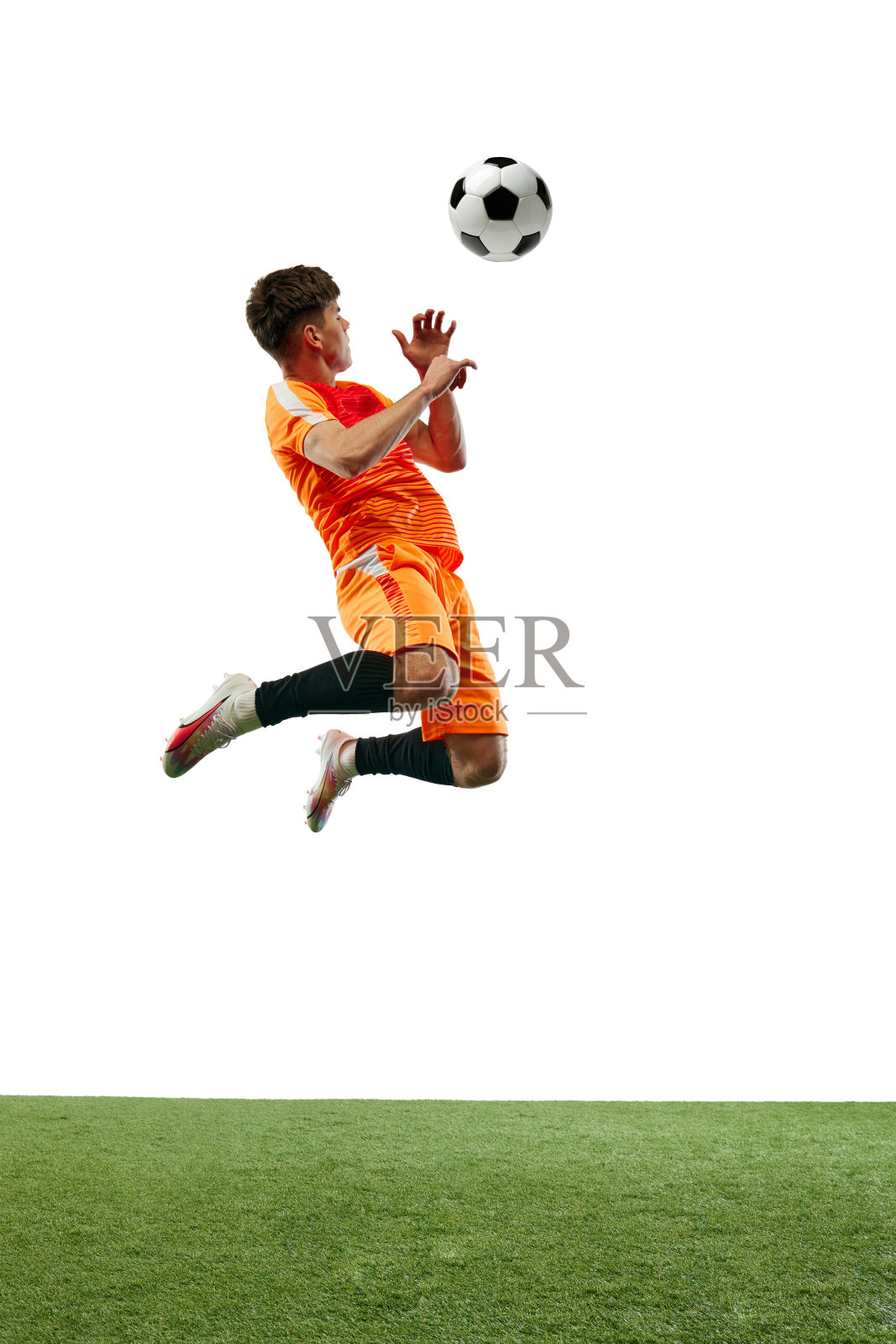 身穿橙色制服的年轻足球运动员在比赛中带球跳跃的全身图像,孤立在白色背景和草地地板上照片摄影图片