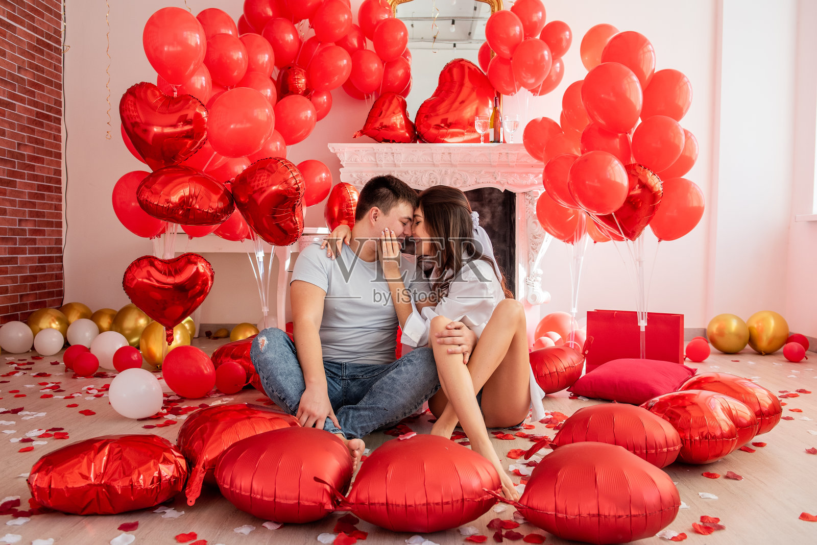 年轻男女紧挨着坐在装饰着红气球的壁炉旁照片摄影图片