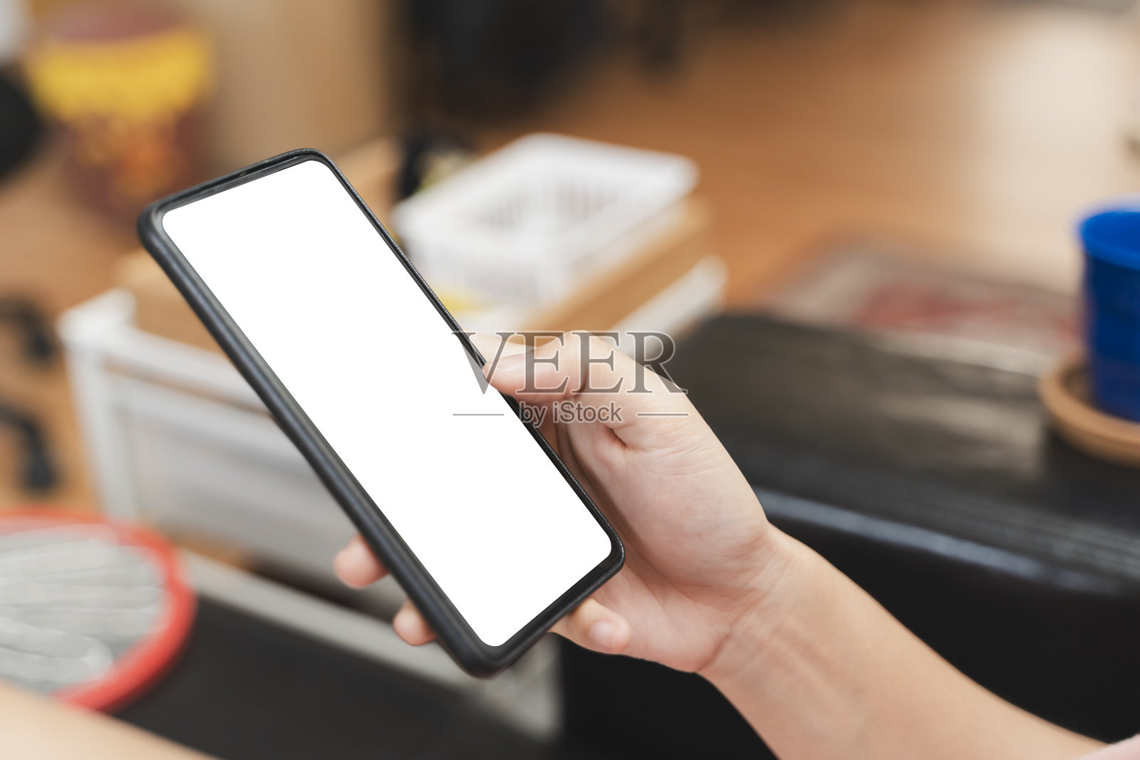 一个穿着牛仔裤的女人坐在咖啡馆里放松地使用她的智能手机。智能手机白屏模型。照片摄影图片