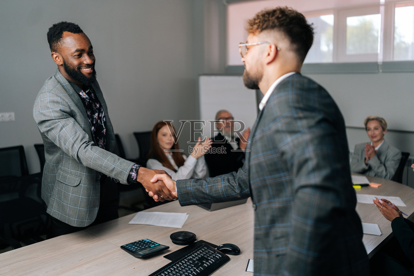 (后景)非洲裔美国人和白人商人在集体谈判中签订合同后愉快地握手,赢得了团队的掌声照片摄影图片