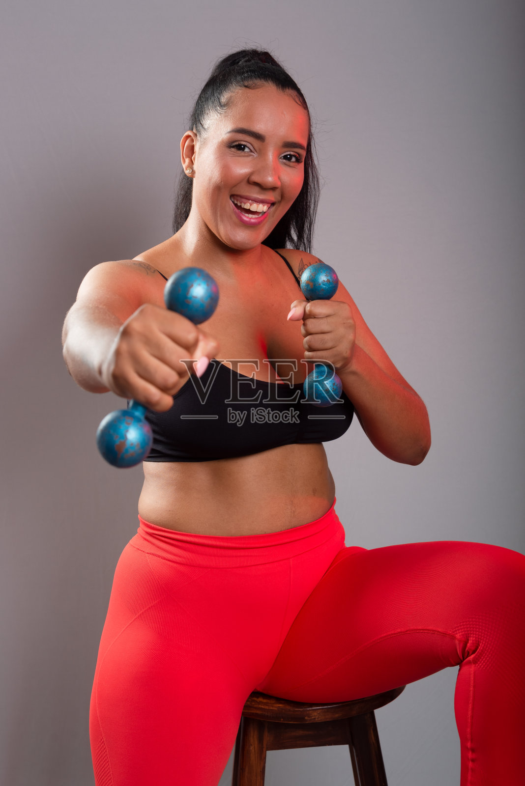 美丽,黑发,快乐,微笑的女人,穿着运动服,拿着哑铃,看着镜头。健康的生活。照片摄影图片