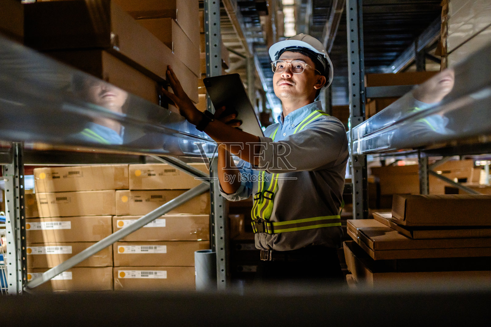 商人或经理使用数字平板电脑查看大型仓库货架上的库存,智能仓库管理系统,供应链和物流网络技术概念。照片摄影图片