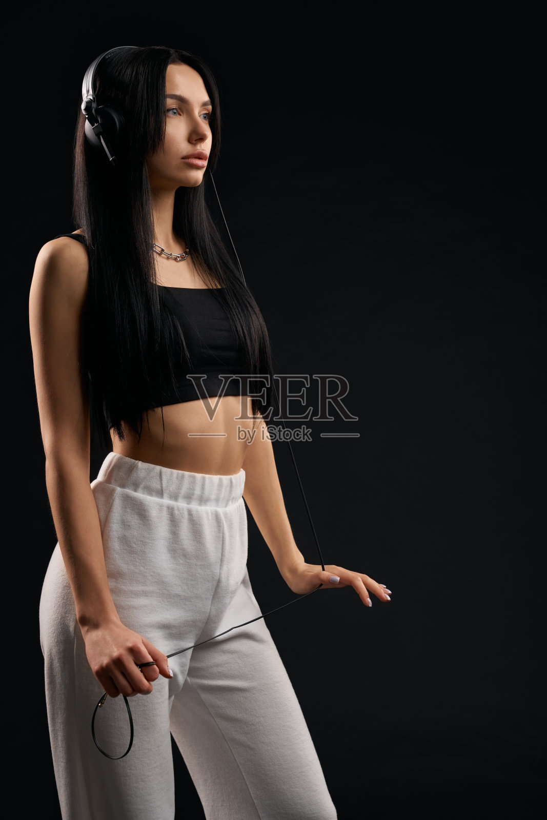 严肃的女士穿着黑色露脐上衣,看着别处,同时在室内听音乐。照片摄影图片