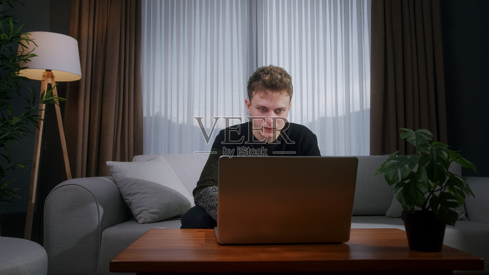 英俊的金发男人通过笔记本电脑进行视频通话,分享新闻,与生活在国外的家人交谈,坐在家里的沙发上享受网络聊天虚拟会议照片摄影图片