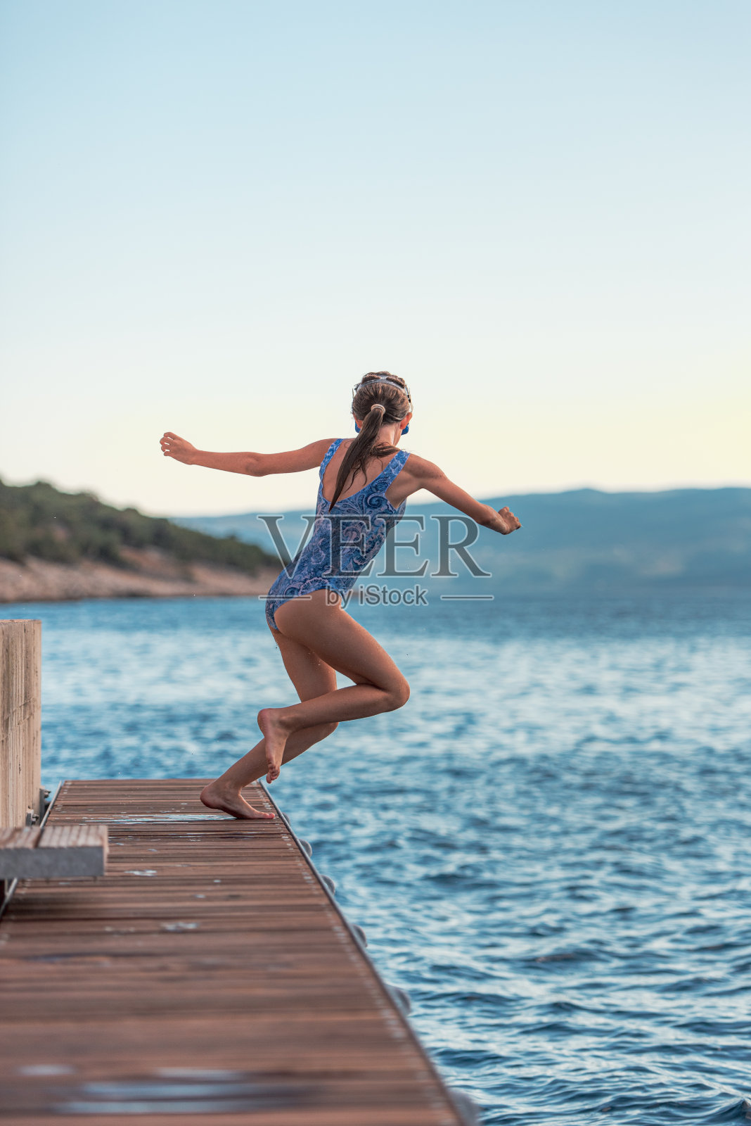 暑假在地中海练习从木码头跳下来的运动姿势的少女照片摄影图片