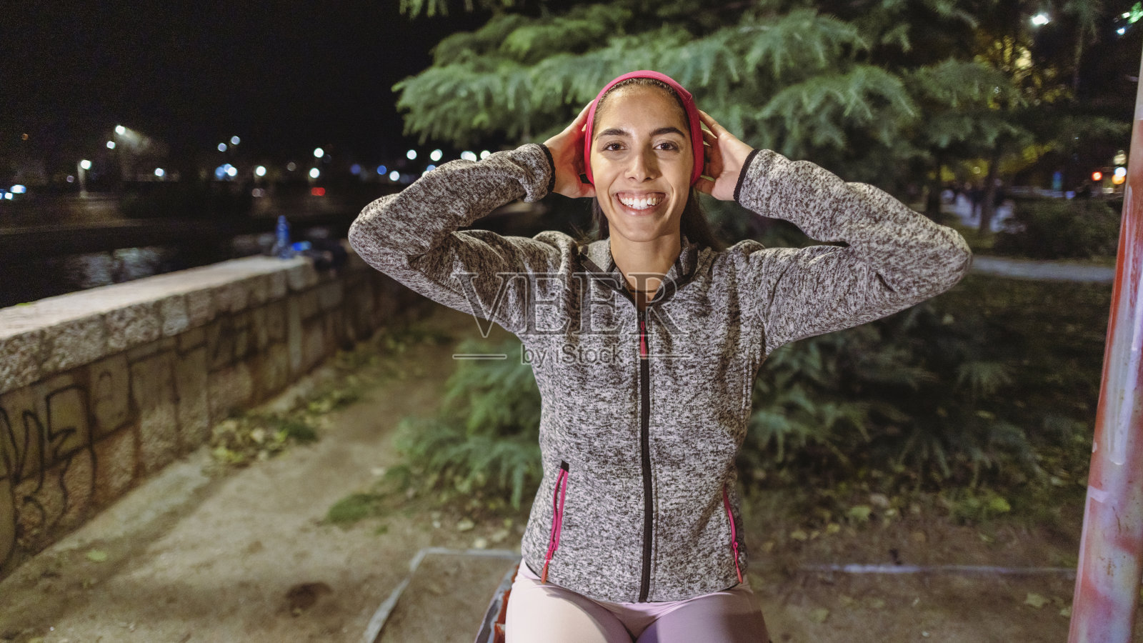 一个活跃的拉丁裔妇女的肖像,在户外健身机上做仰卧起坐,在晚上照片摄影图片