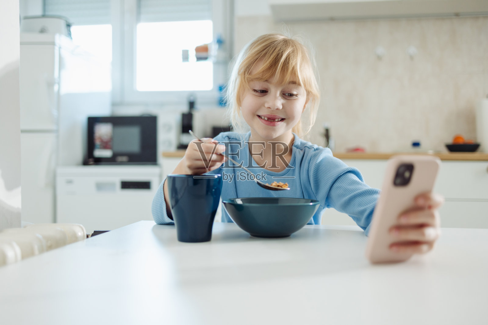 小女孩在家厨房边吃早餐边打电话照片摄影图片