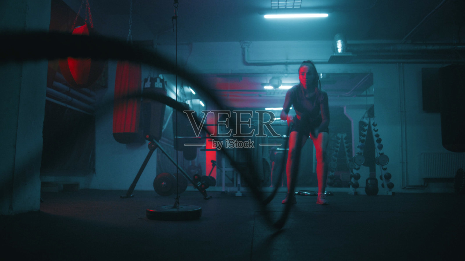 女运动员在黑暗的拳击馆里用战斗绳练习照片摄影图片