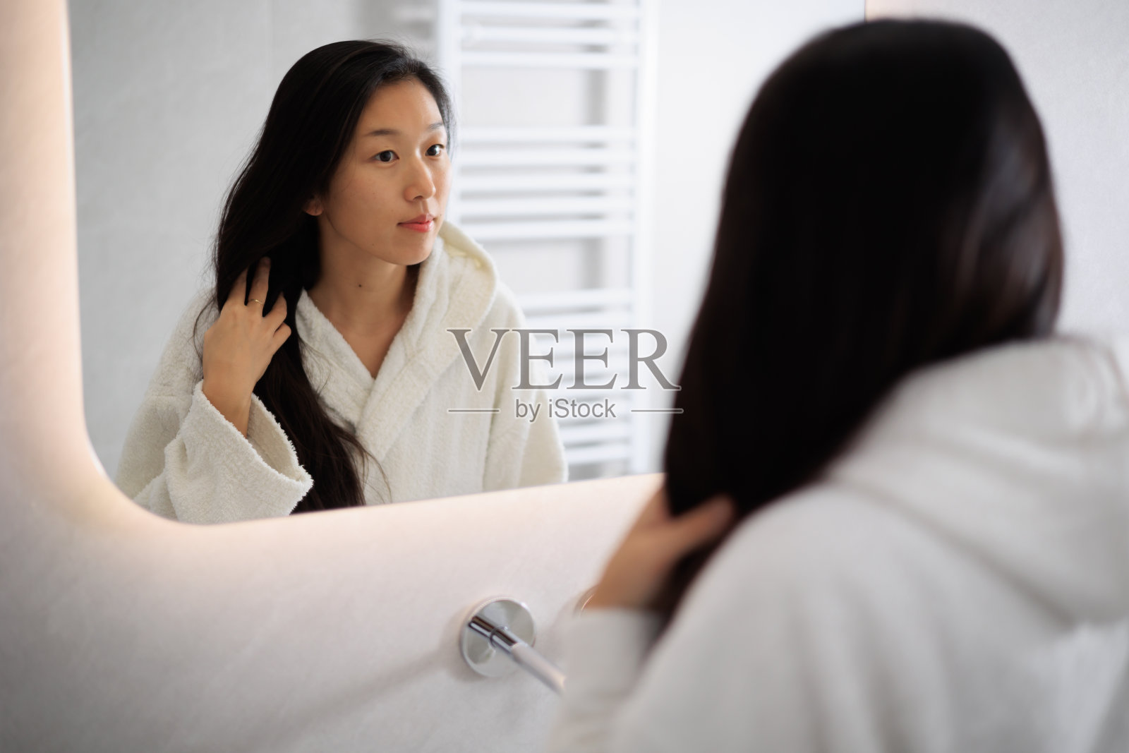 美丽的年轻亚洲女人看着她在镜子里,照顾她的皮肤和头发照片摄影图片