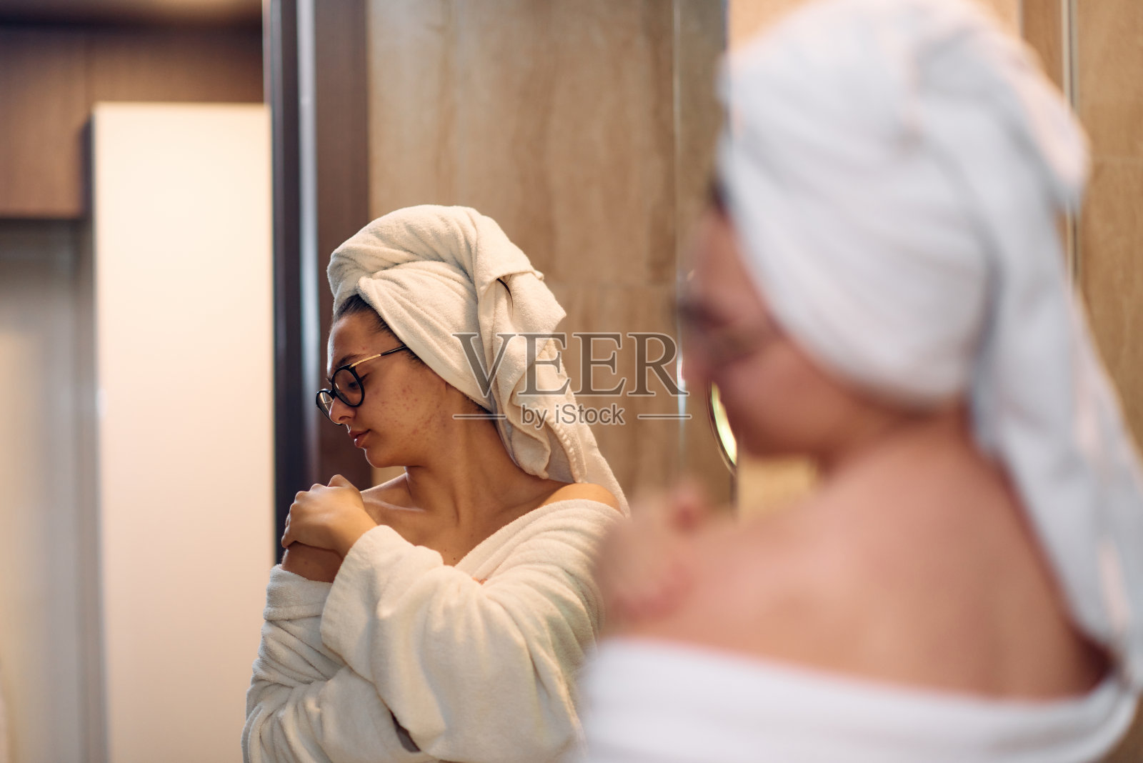 一个女人在放松的沐浴后优雅地将滋润的保湿霜涂抹在她的肩膀上,体现了一个容光焕发和恢复活力的护肤程序照片摄影图片