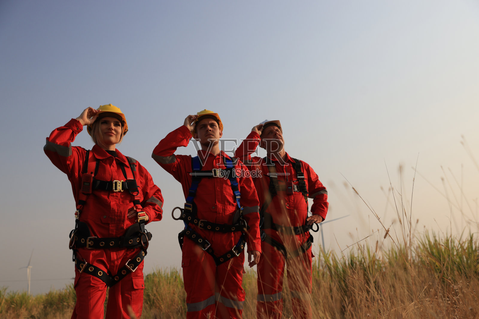 肖像风车工程师团队与红色安全制服和安全带在风力涡轮机农场前照片摄影图片