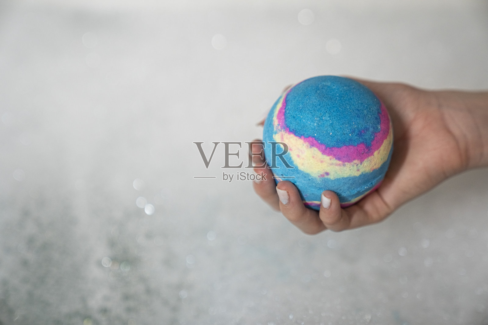 女性的手,水溶性蓝色,黄色,粉色,沐浴炸弹,气泡水,近距离。照片摄影图片