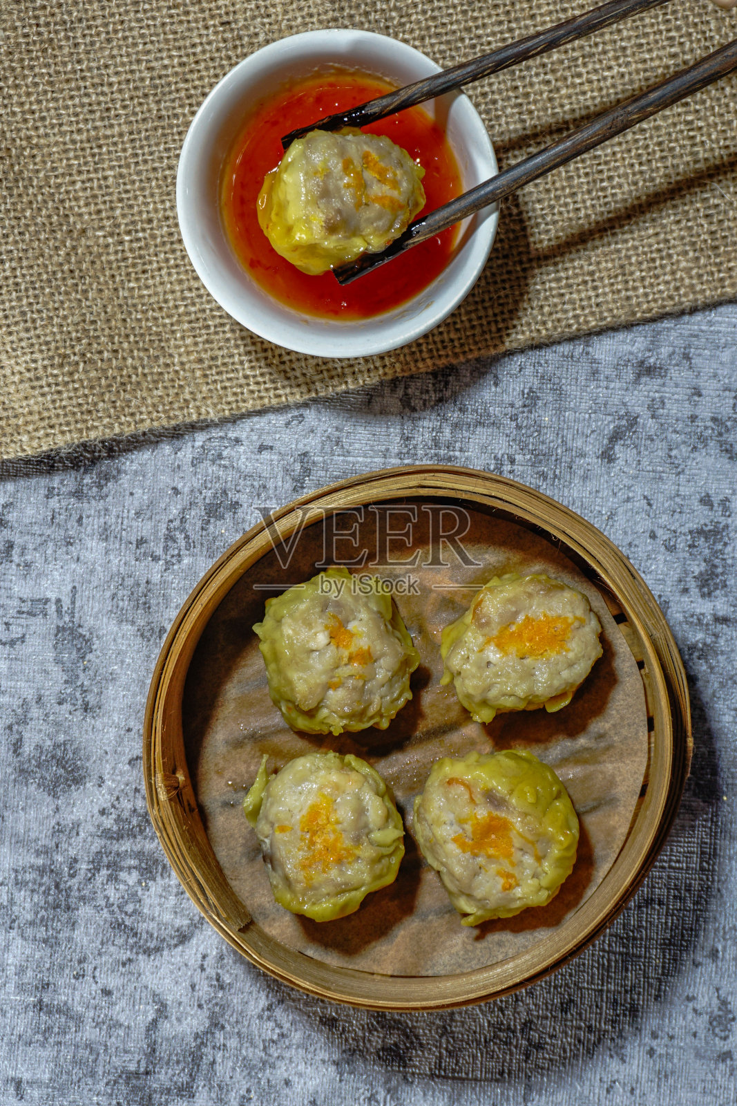 蒸饺烧麦放在竹篮蒸笼里,蘸酱和筷子放在灰色的背景上。平的。照片摄影图片