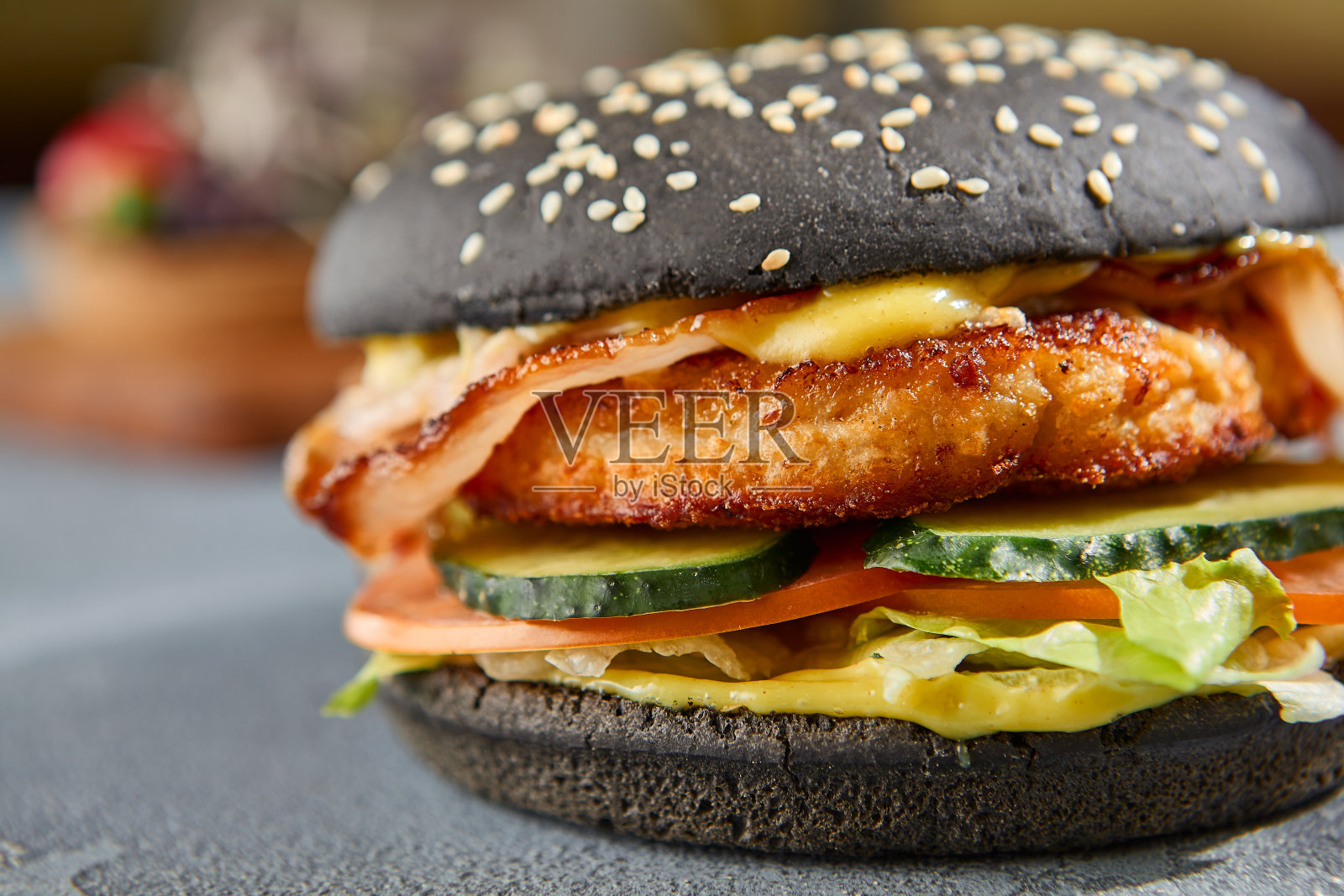 黑色圆面包上的鸡肉和培根汉堡的特写水平捕捉,揭示了丰富的纹理。灰色的混凝土背景和粗糙的阴影完成了美学照片摄影图片