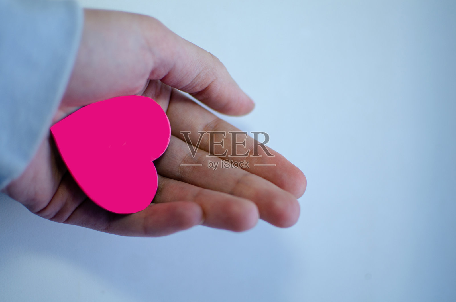 一个女人手里拿着一颗粉红色的心,背景是蓝色的照片摄影图片