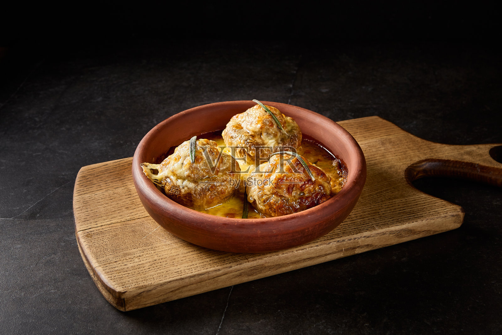 在一个质朴的粘土盘子里塞满肉的烤蘑菇,在一个极简主义的黑色背景下,漂亮地摆在木板上,展示了传统的格鲁吉亚美食照片摄影图片