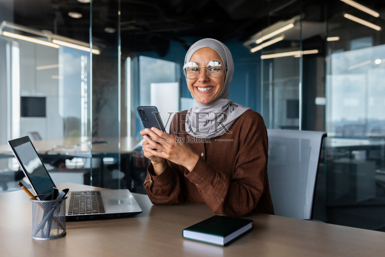 戴着头巾在办公室用笔记本电脑工作的微笑的年轻穆斯林妇女照片摄影图片