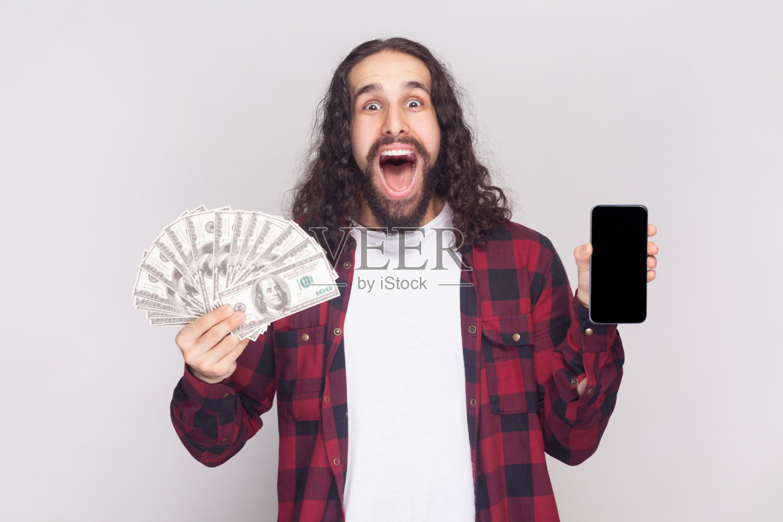 惊讶兴奋的络腮胡男人拿着美元钞票和带有空白模型的手机照片摄影图片