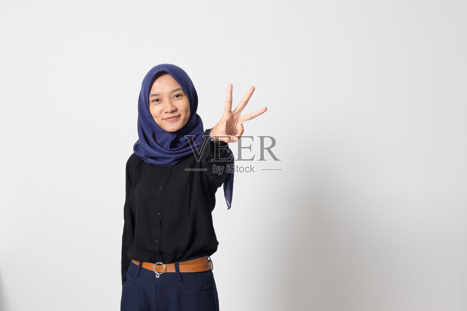 穿着休闲西装的亚洲头巾妇女的肖像,露出并指向第三个手指,同时微笑着自信和快乐。商人的概念。白色背景上的孤立图像照片摄影图片