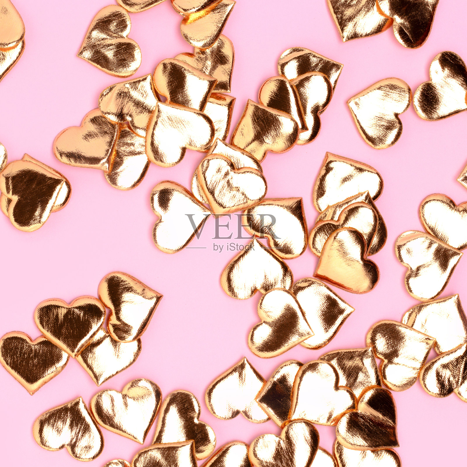 金色的心形纸屑散落在粉红色的背景上。照片摄影图片