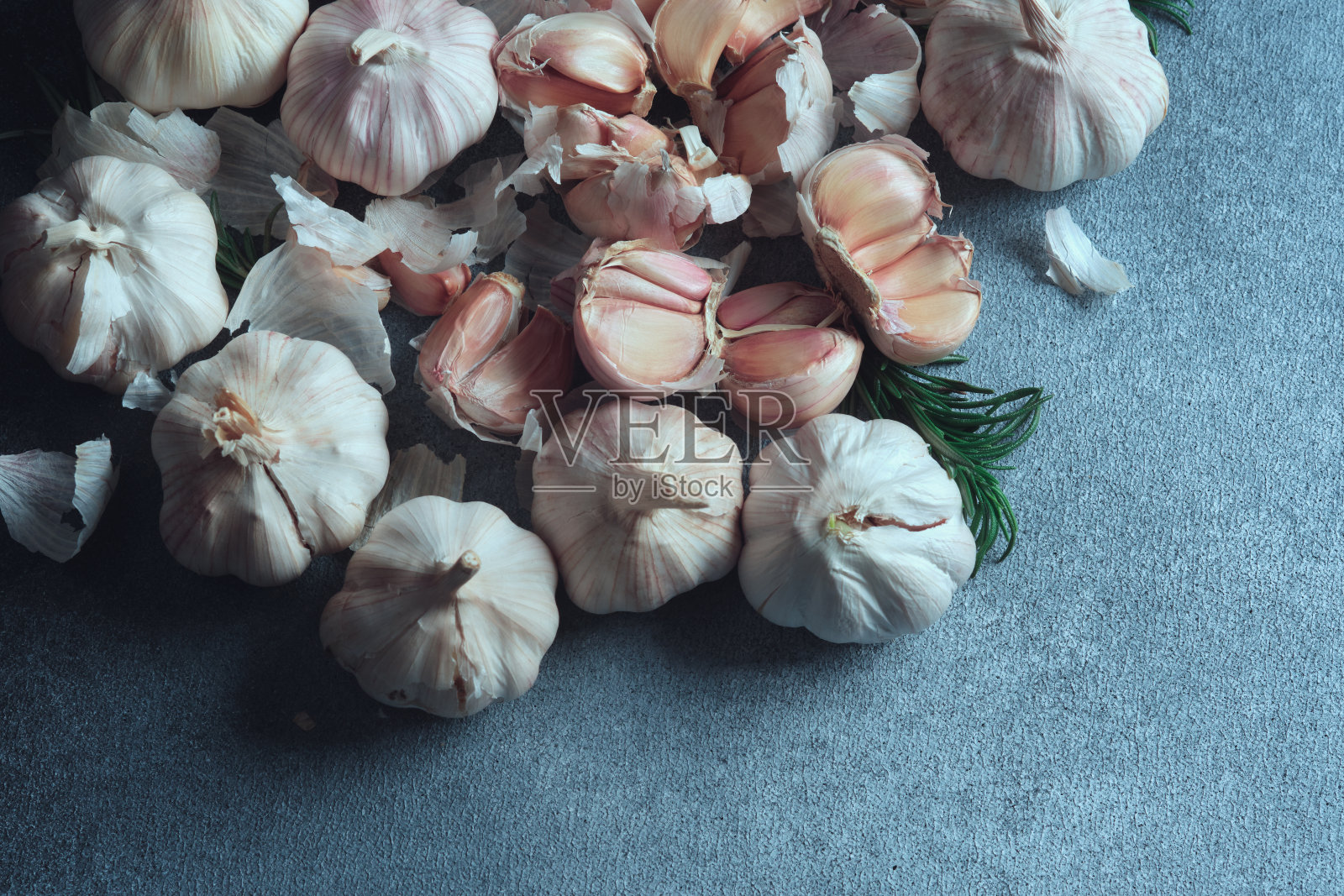 大蒜球茎和丁香的深色纹理组成。头顶上的大蒜鳞茎和单个丁香,辅以迷迭香,在黑暗的纹理表面。照片摄影图片