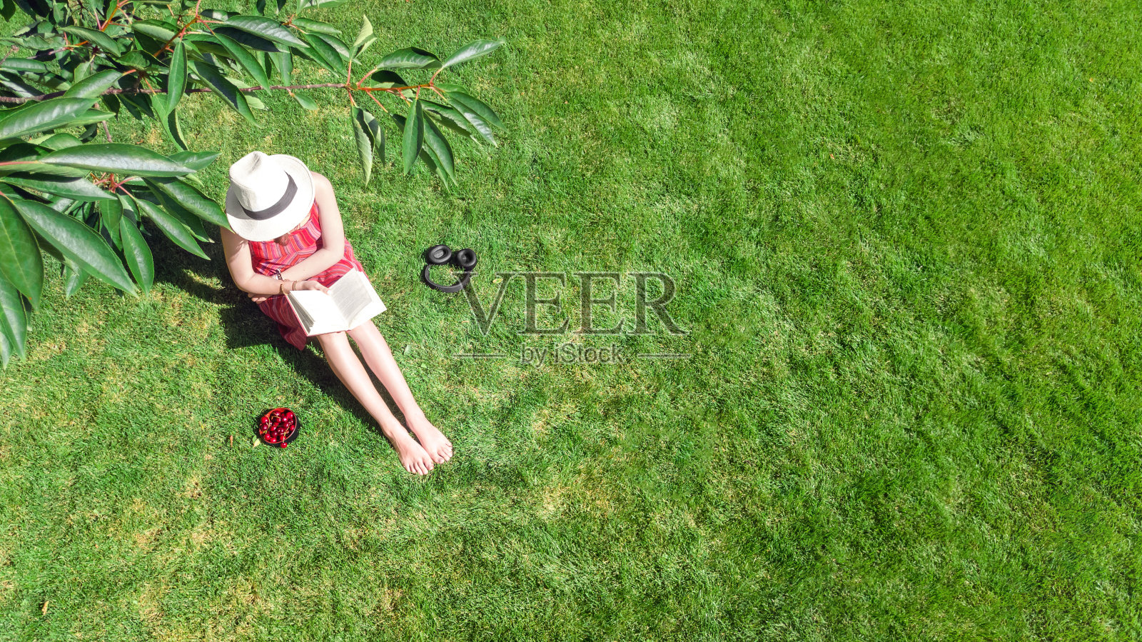 年轻女子在自行车旁的公园看书。一个女学生拿着书和耳机坐在户外的草地上放松,无人机从上面俯瞰照片摄影图片