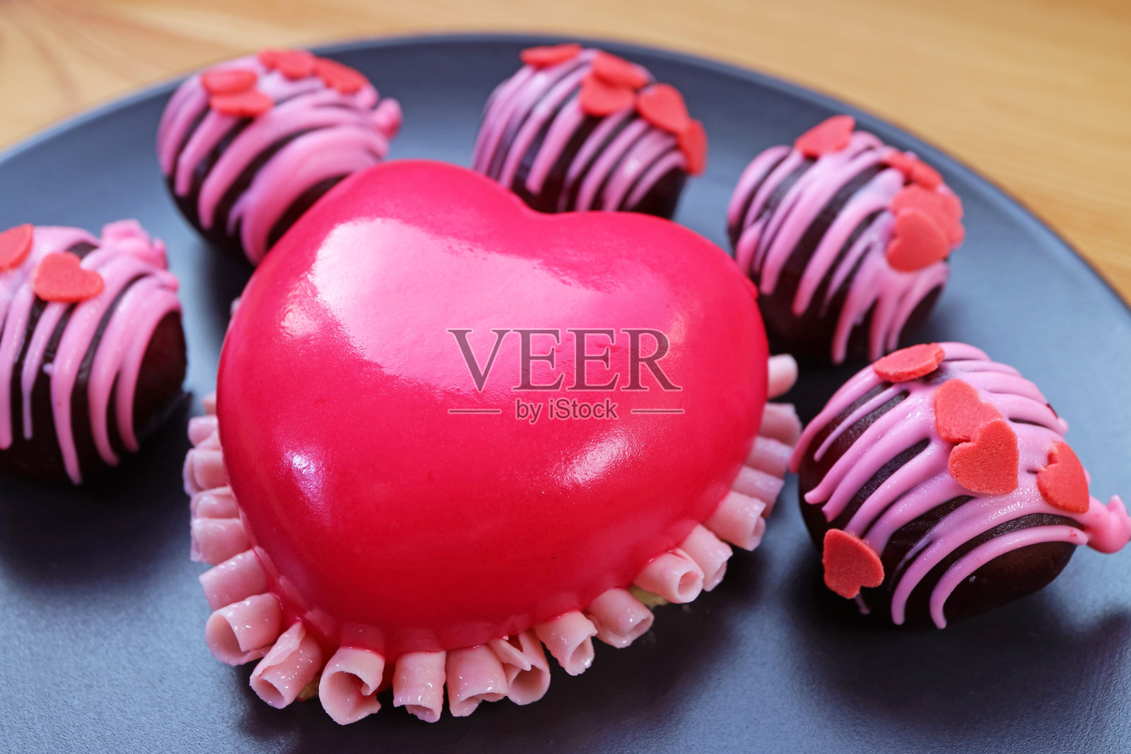 黑色盘子上生动的粉色心形草莓慕斯蛋糕与巧克力蛋糕球的特写照片摄影图片