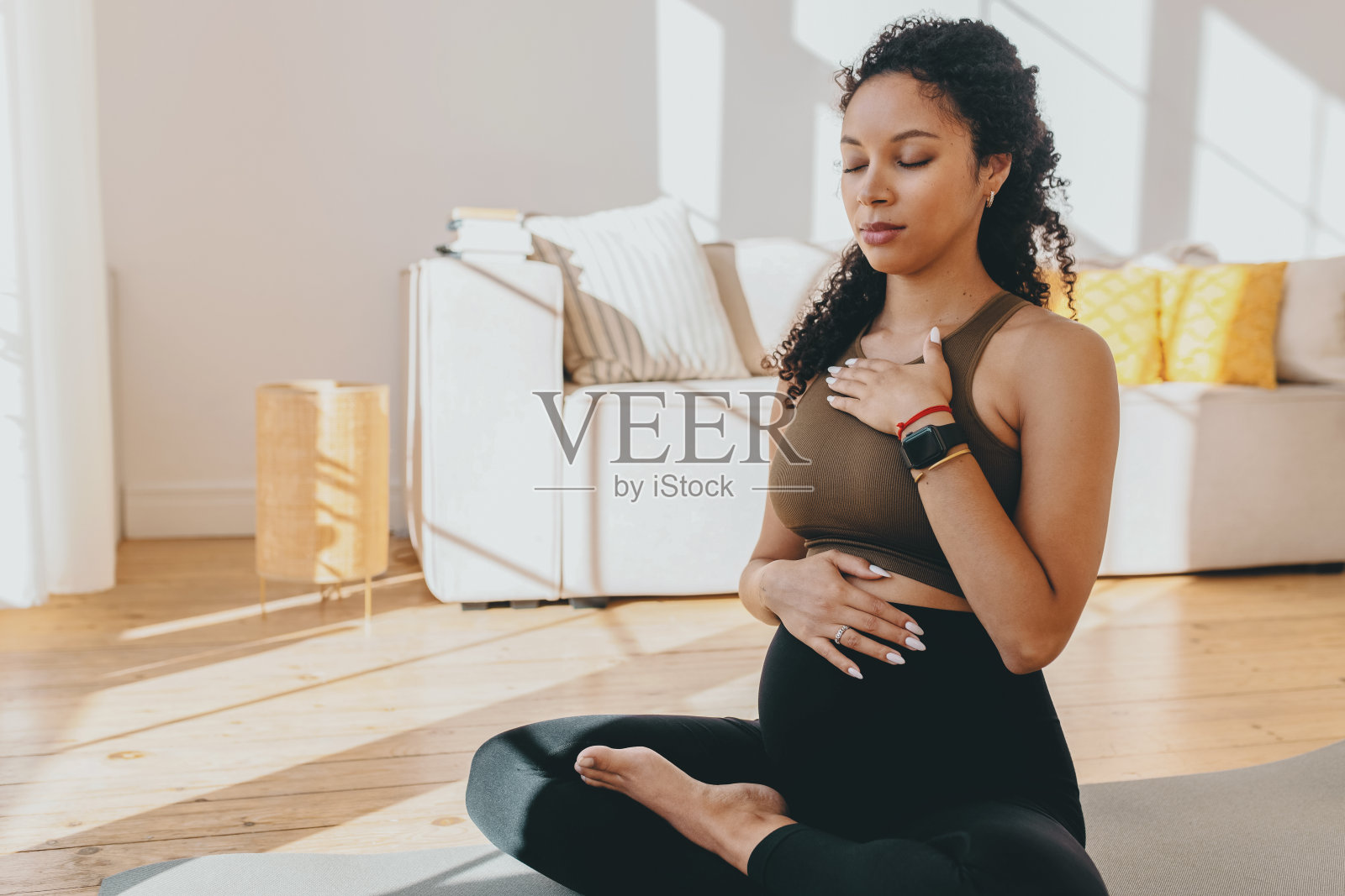 一个非洲裔美国孕妇,闭着眼睛坐在垫子上,深呼吸,练习瑜伽和调息技巧,把手放在胸部和腹部,为分娩做准备照片摄影图片